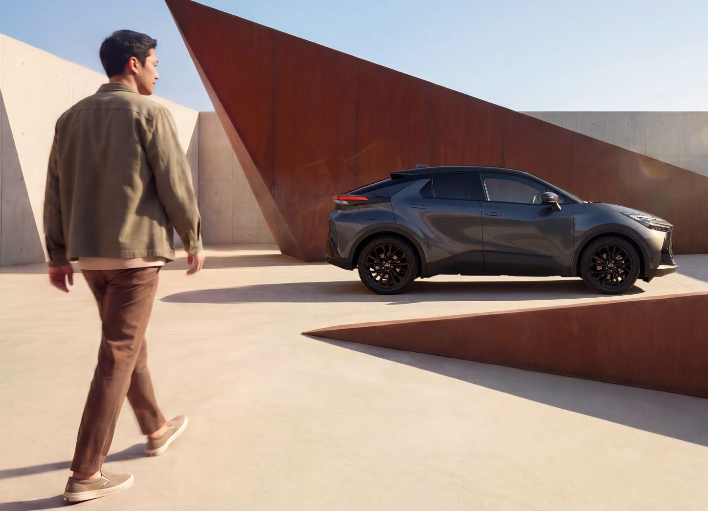 Ein Toyota C-HR steht vor moderner Architektur, während eine Person auf das Fahrzeug zugeht.